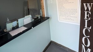 A reception desk with a 'Welcome' sign, a framed notice with check-in times and policies, and a mirror reflecting part of the room. - SE'Air Motel By Townhouse Corpus Christi / Padre Island Tx (Corpus Christi)