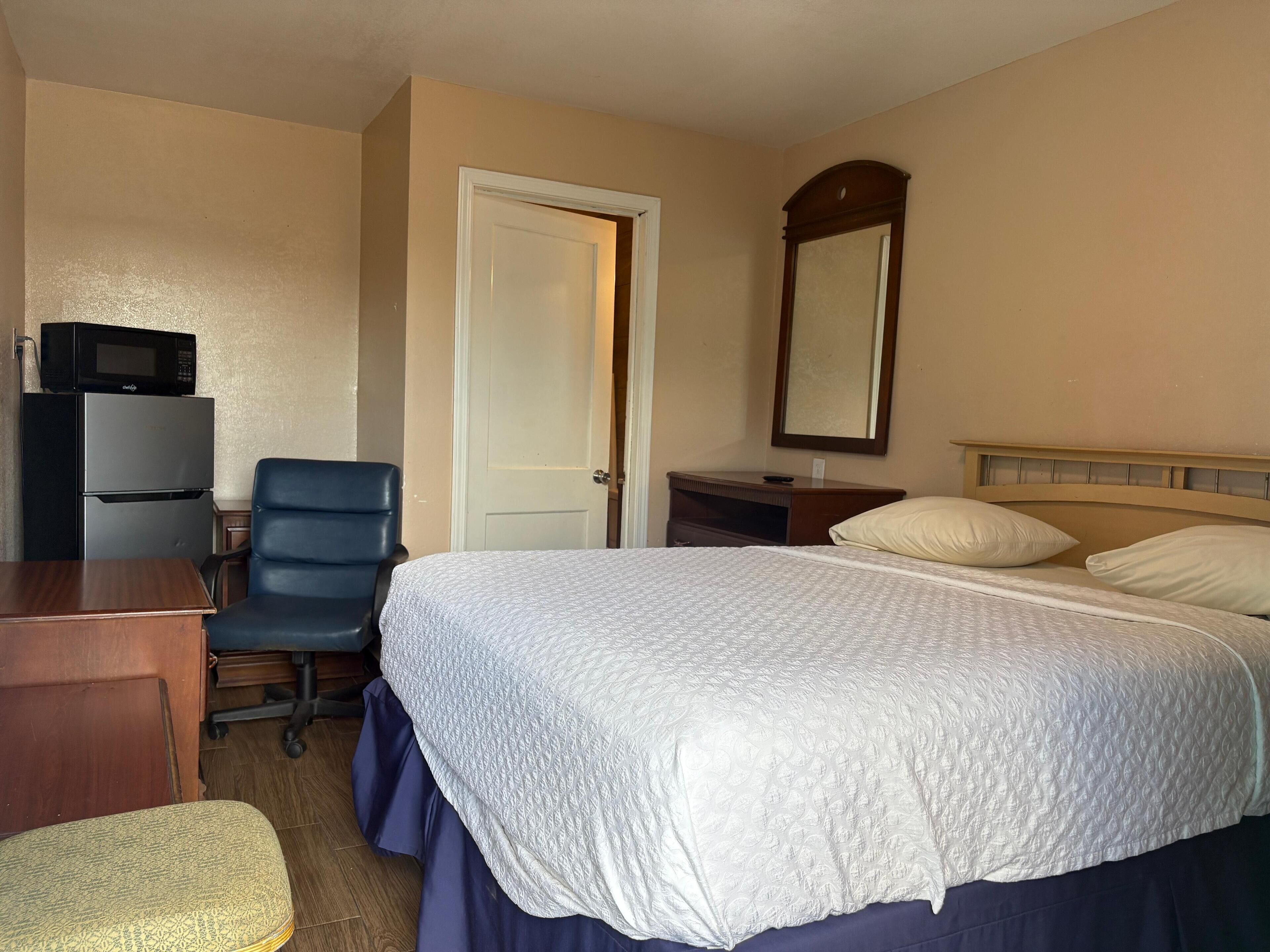 A hotel room with a bed, a desk with a chair, a microwave, and a refrigerator.