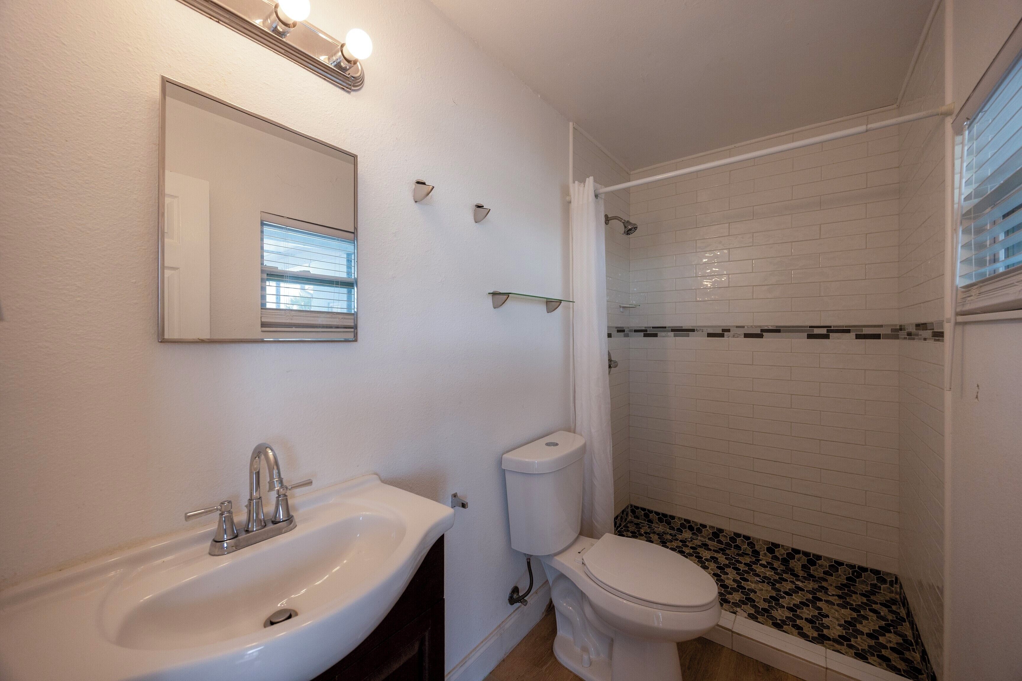 A bathroom with a white sink, a toilet, and a shower area with tiled walls and a black and white patterned floor.