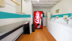 Une buanderie équipée d’un distributeur automatique de Coca-Cola, d’une poubelle et d’un lave-linge.