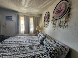 Une chambre avec une couvre-lit à motifs, des rideaux, un attrape-rêves fixé au mur et une lampe.