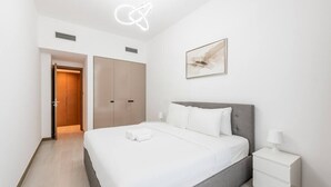 A modern hotel room with a large bed, a bedside table, a nightstand, a ceiling light fixture, and a door leading to another room. - River Views next to Burj Khalifa (Dubai)