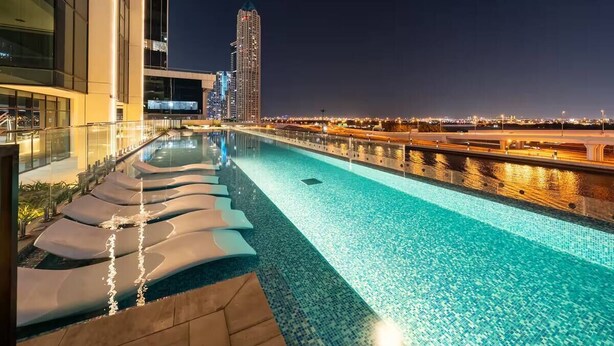 A nighttime pool area with lounge chairs and a view of a city skyline. - River Views next to Burj Khalifa (Dubai)