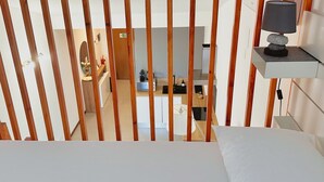 Een kamer met een bed, een houten lattenwand, een wastafel en een klein tafeltje met een lamp.