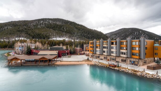 Un hôtel situé au bord de l’eau, doté d’un quai, de bâtiments avec des balcons et surplombant un paysage montagneux.