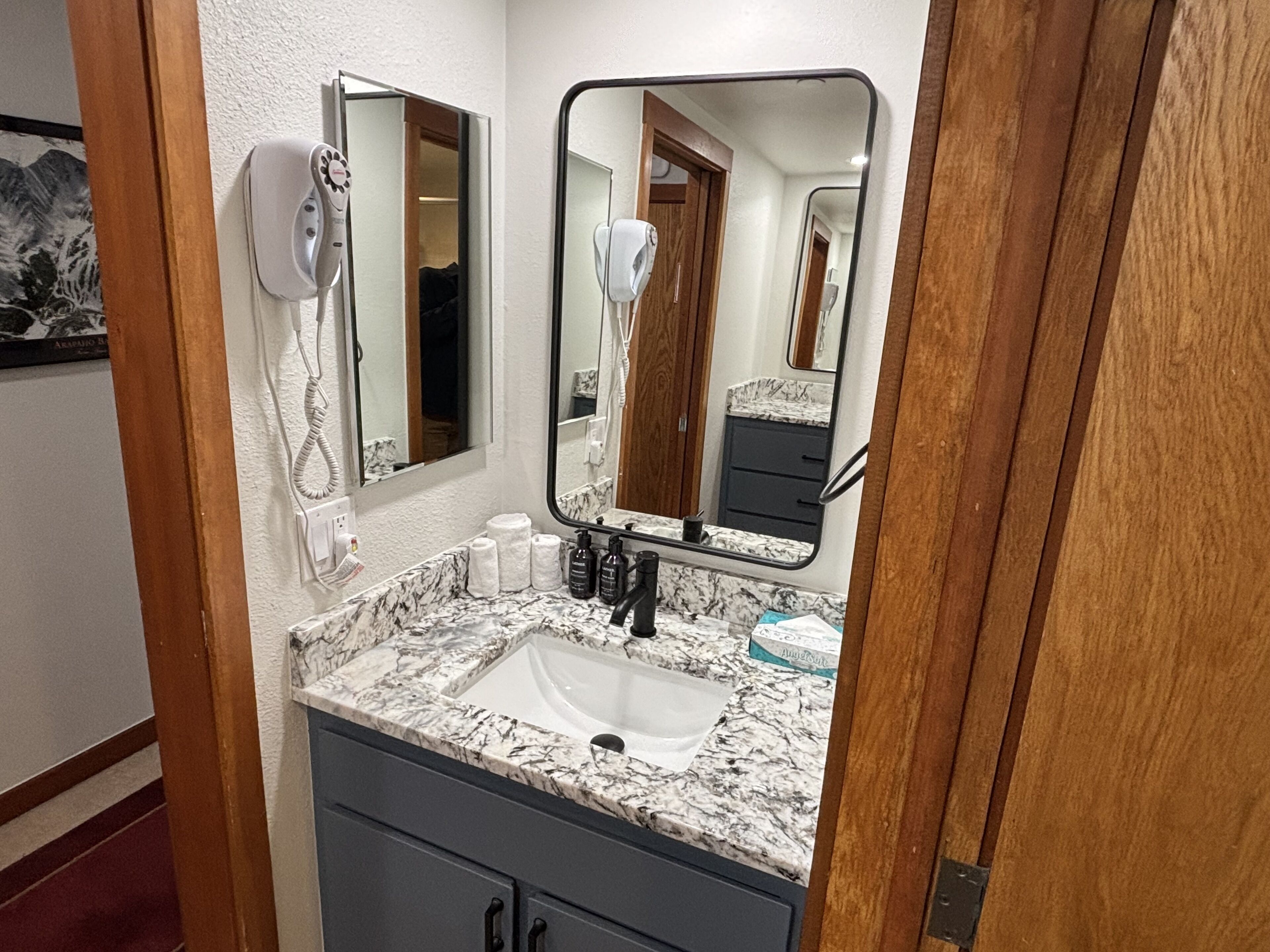 A bathroom with a marble sink, a hairdryer, and a mirror.