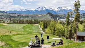 Un parcours de golf avec une chaîne de montagnes en arrière-plan, un chalet et un ciel dégagé.