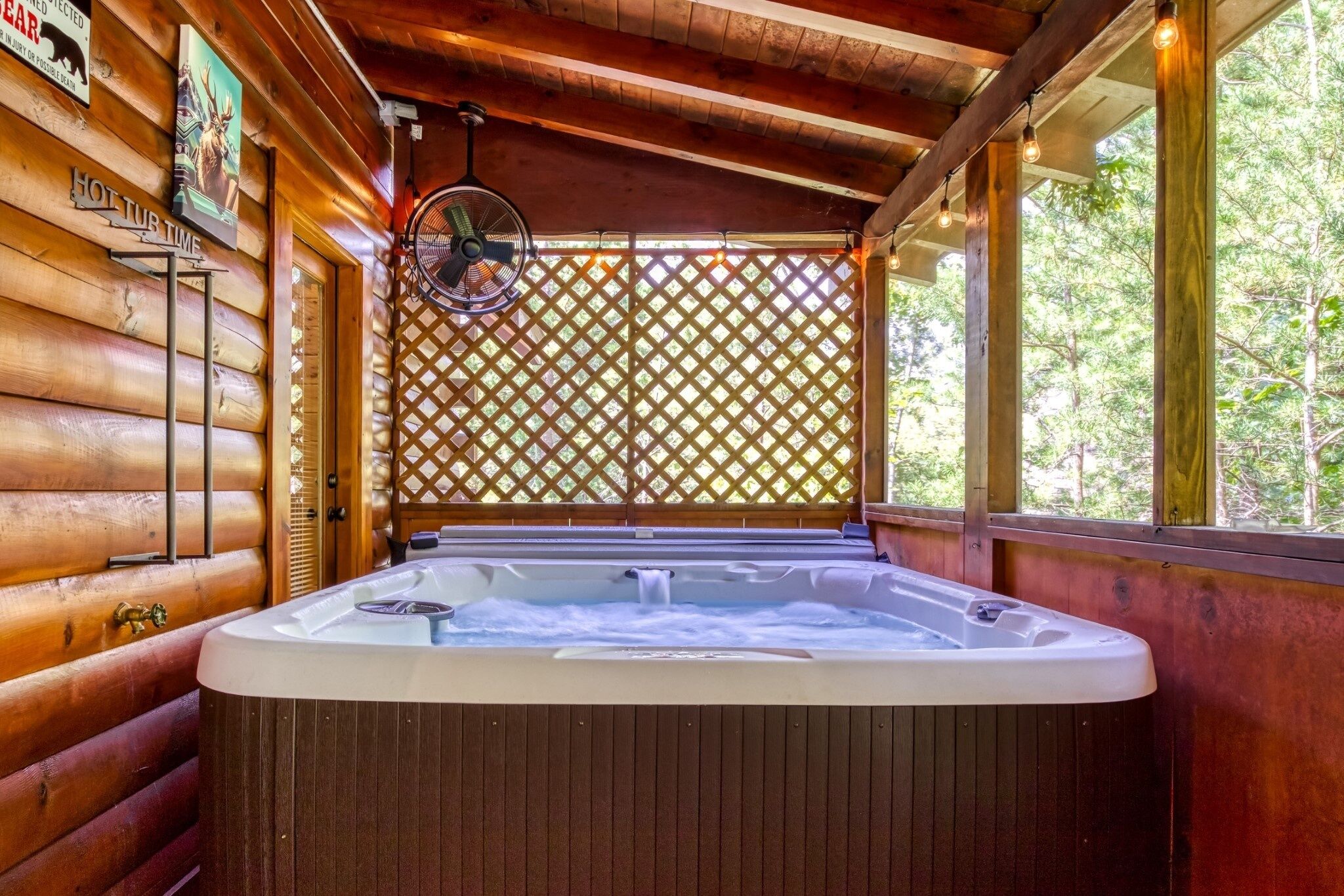 A wooden cabin interior with a hot tub, a fan, and a lattice screen.