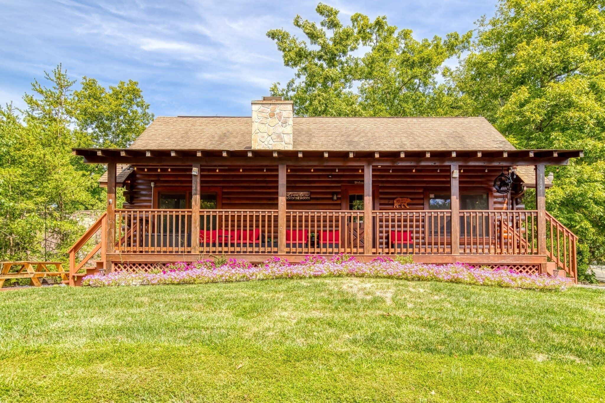 A log cabin with a covered porch, a stone chimney, and a red bench.