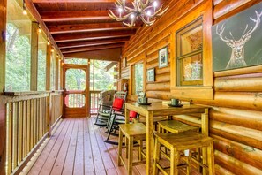 Uma cabana de madeira com varanda, uma mesa de jantar e cadeiras.