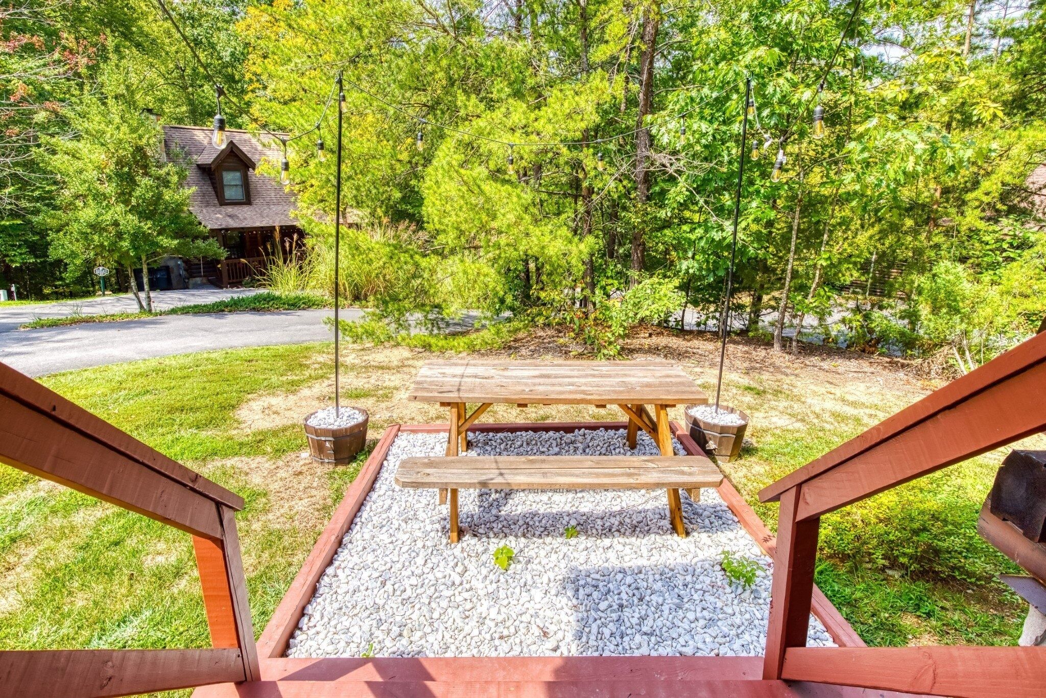 A wooden picnic table with benches in a gravel area surrounded by trees.