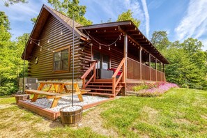 Uma cabana de toras com varanda, mobiliário de exterior e lareira de pedra.