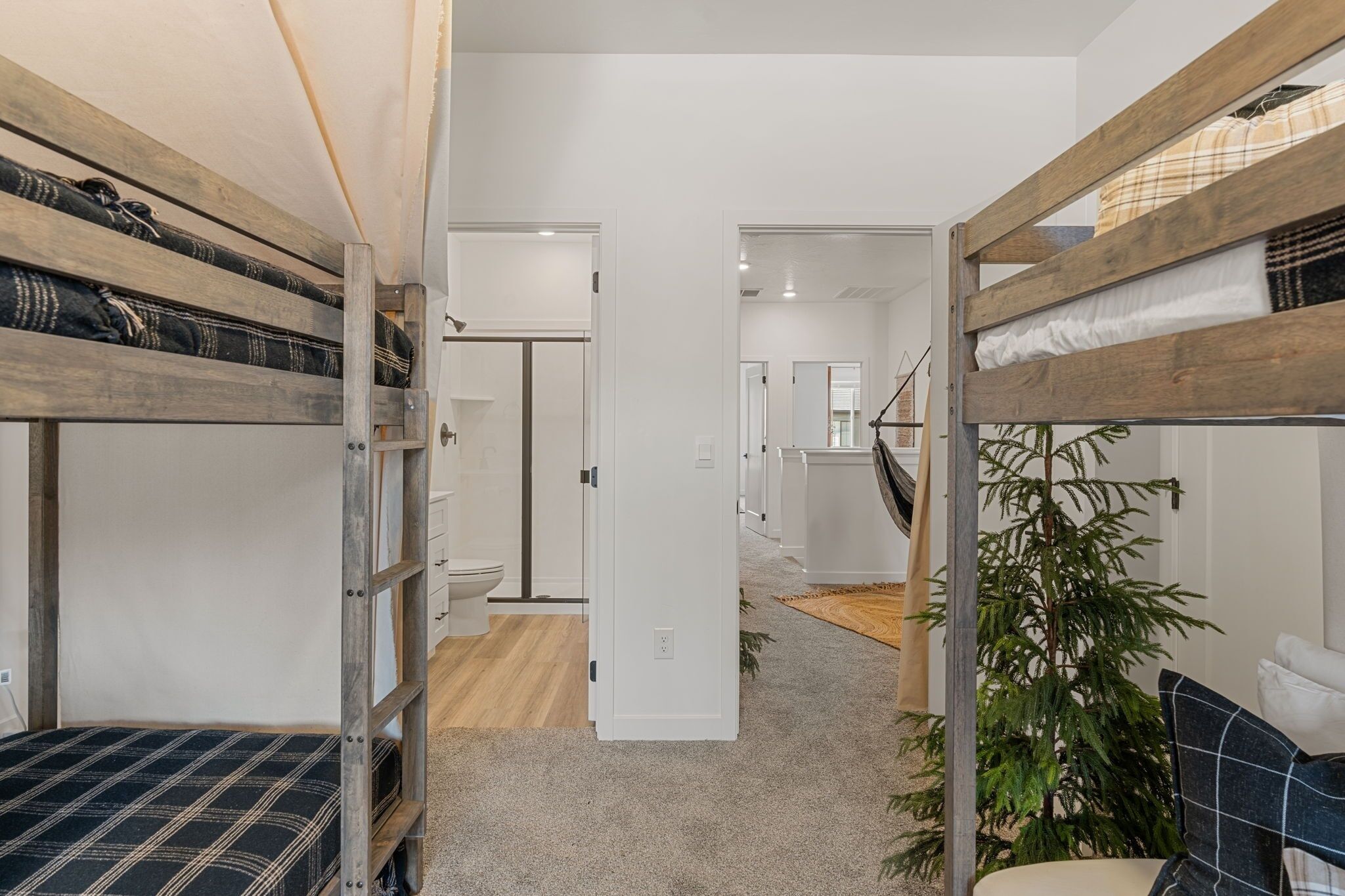 A compact, modern room with bunk beds, a white door, a small plant, and a staircase leading to another area.