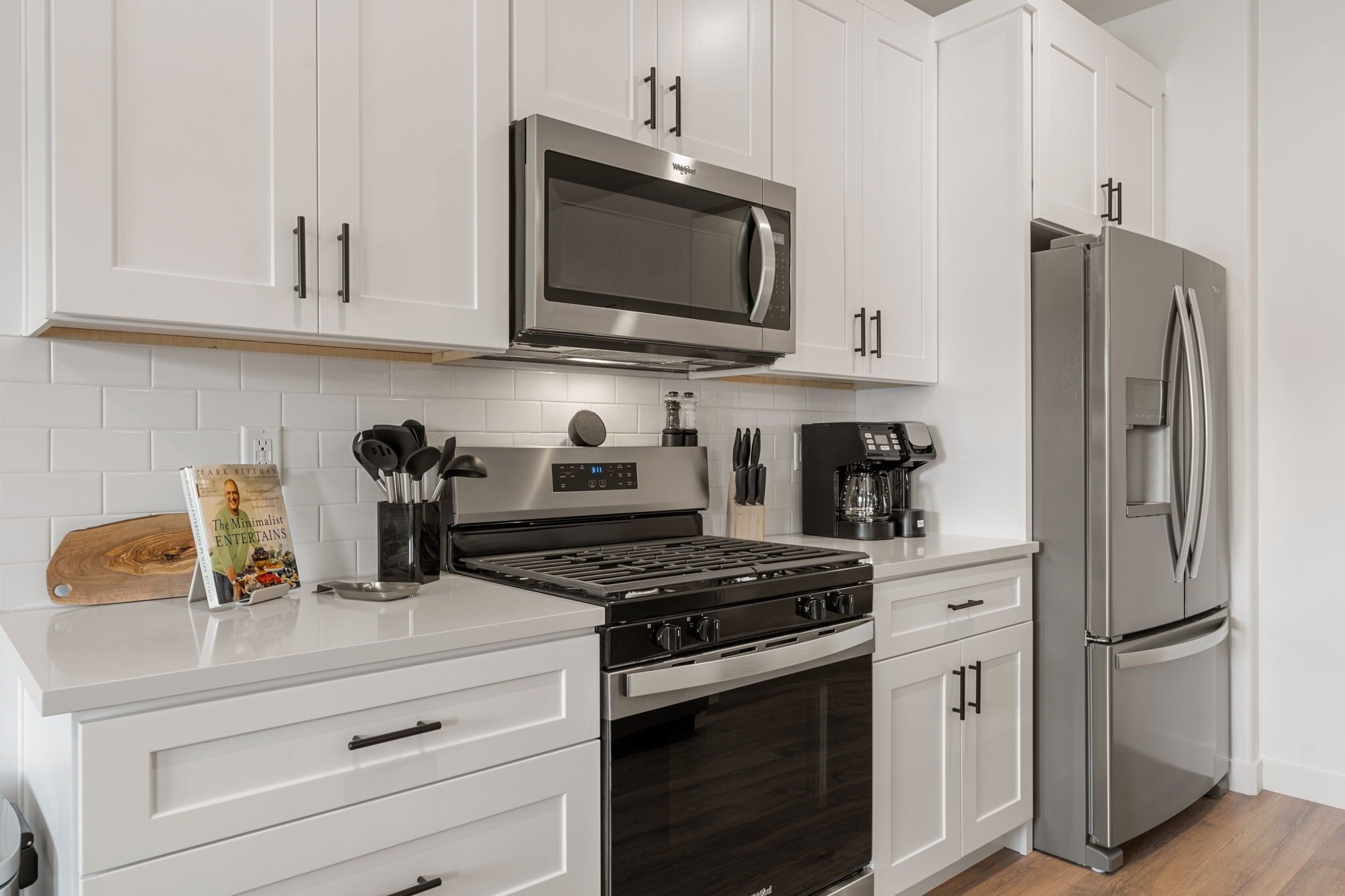 A modern kitchen with white cabinetry, a stainless steel microwave, a double-door refrigerator, and a gas stove.