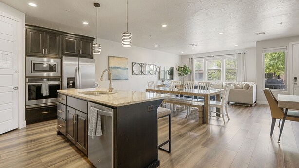 A modern kitchen with stainless steel appliances, a central island, pendant lighting, and a dining area with a view of the outdoors. - Relax In Style 4 Bedroom Townhouse (Washington)