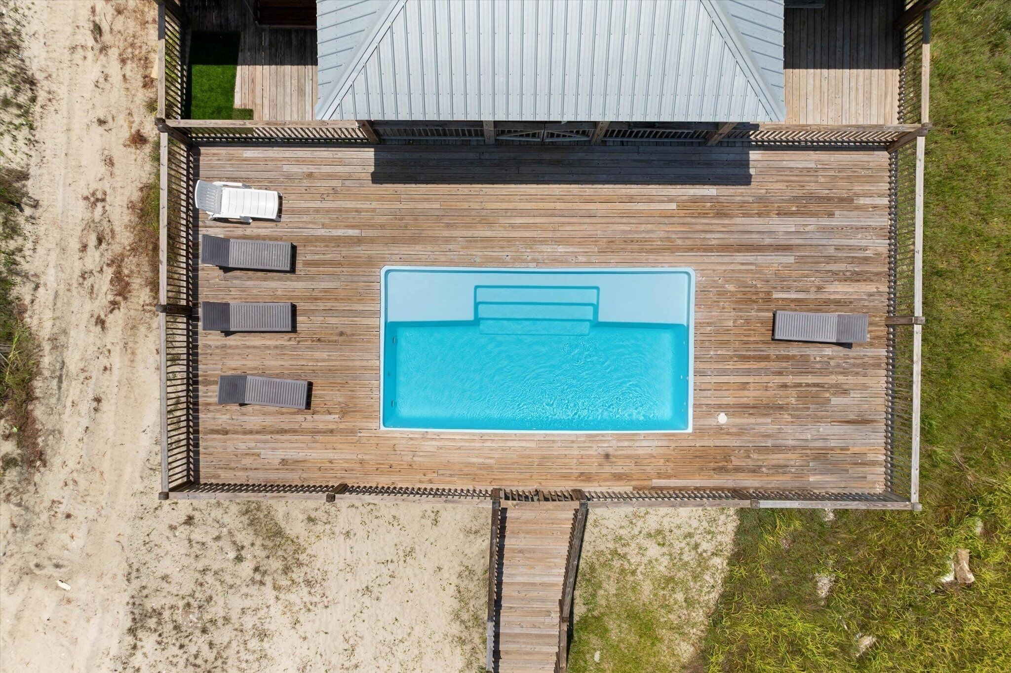 Vista aérea de una terraza de madera con una piscina, rodeada de sillas de descanso y una zona cubierta.