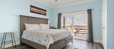 A bedroom with a bed, a ceiling fan, a nightstand, a window with curtains, and a view of an outdoor deck.