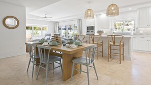 Une cuisine spacieuse avec des meubles blancs, une table à manger en bois et un grand îlot central doté de sièges.