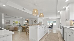 Une cuisine spacieuse avec des meubles blancs, un îlot central et des luminaires suspendus.