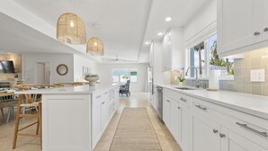 Une cuisine moderne avec des meubles blancs, un îlot central et un coin repas doté de chaises en bois.