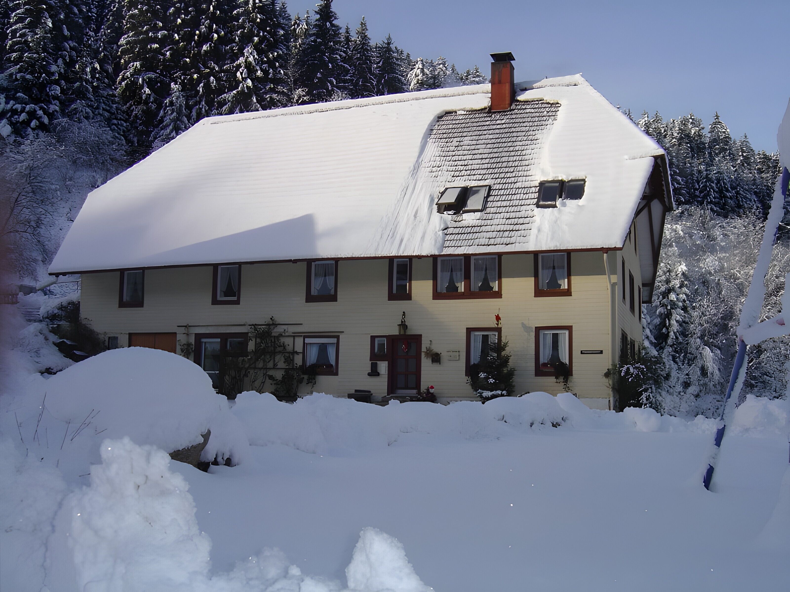 A two-story house with a snow-covered roof and a chimney.