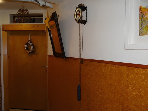 A room with a wooden door, a wall-mounted clock, and a framed picture.