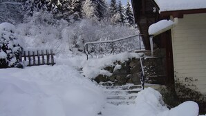 Ett snötäckt utomhusområde med trappsteg som leder upp till en byggnad, ett trästaket och snötyngda träd.