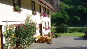 En byggnad med en vit fasad, flera fönster med blomlådor, ett träbord och stolar utomhus samt en asfalterad uppfart.