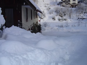 A snow-covered residential area with houses, a fence, and a large snowbank. - Apartment 4, 36 sqm with shared garden and Wi-Fi (Triberg im Schwarzwald)