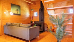 Interior acogedor de una cabaña con sofá, chimenea, paredes de madera y una planta en maceta.