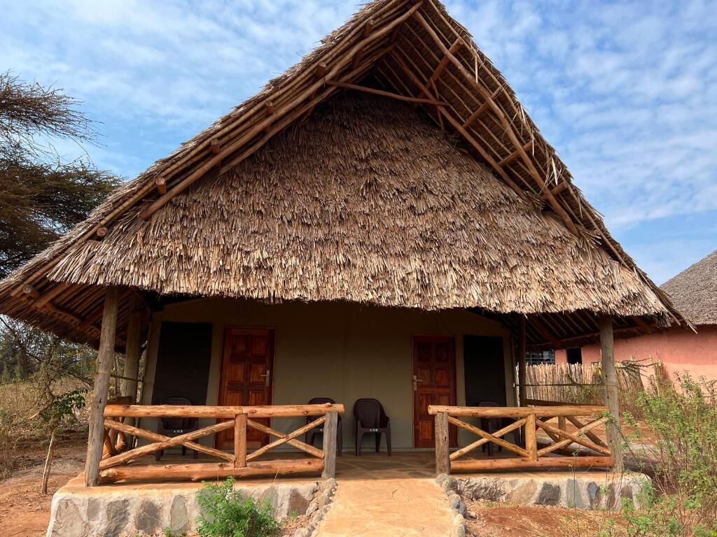 A thatched-roof hut with a wooden porch and a stone pathway leading to the entrance.