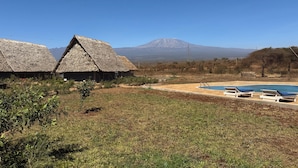 Un resort con cabañas de techo de paja, una piscina y una montaña al fondo.
