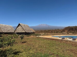 A resort with thatched-roof huts, a swimming pool, and a mountain in the background.