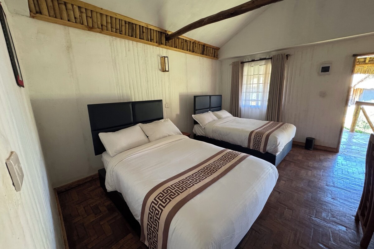 Habitación con dos camas, piso de madera, techo inclinado y ventana con cortinas.