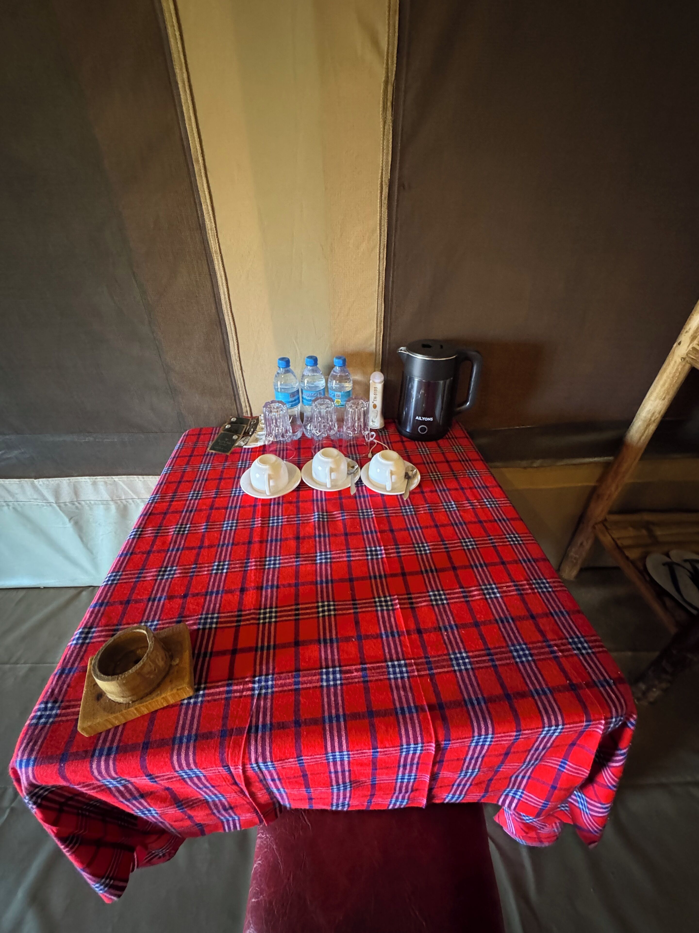 A table with a red plaid tablecloth, water bottles, a kettle, and a wooden cup.