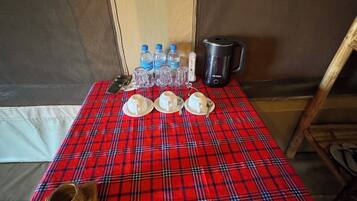 A table with a red plaid tablecloth, water bottles, a kettle, and a wooden cup.