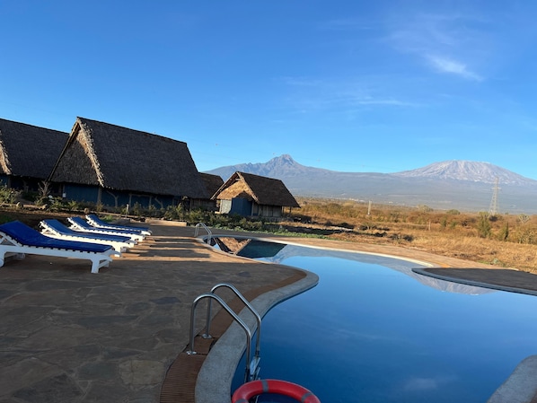 Zona de piscina con sillones de descanso y una vista despejada de una montaña al fondo.