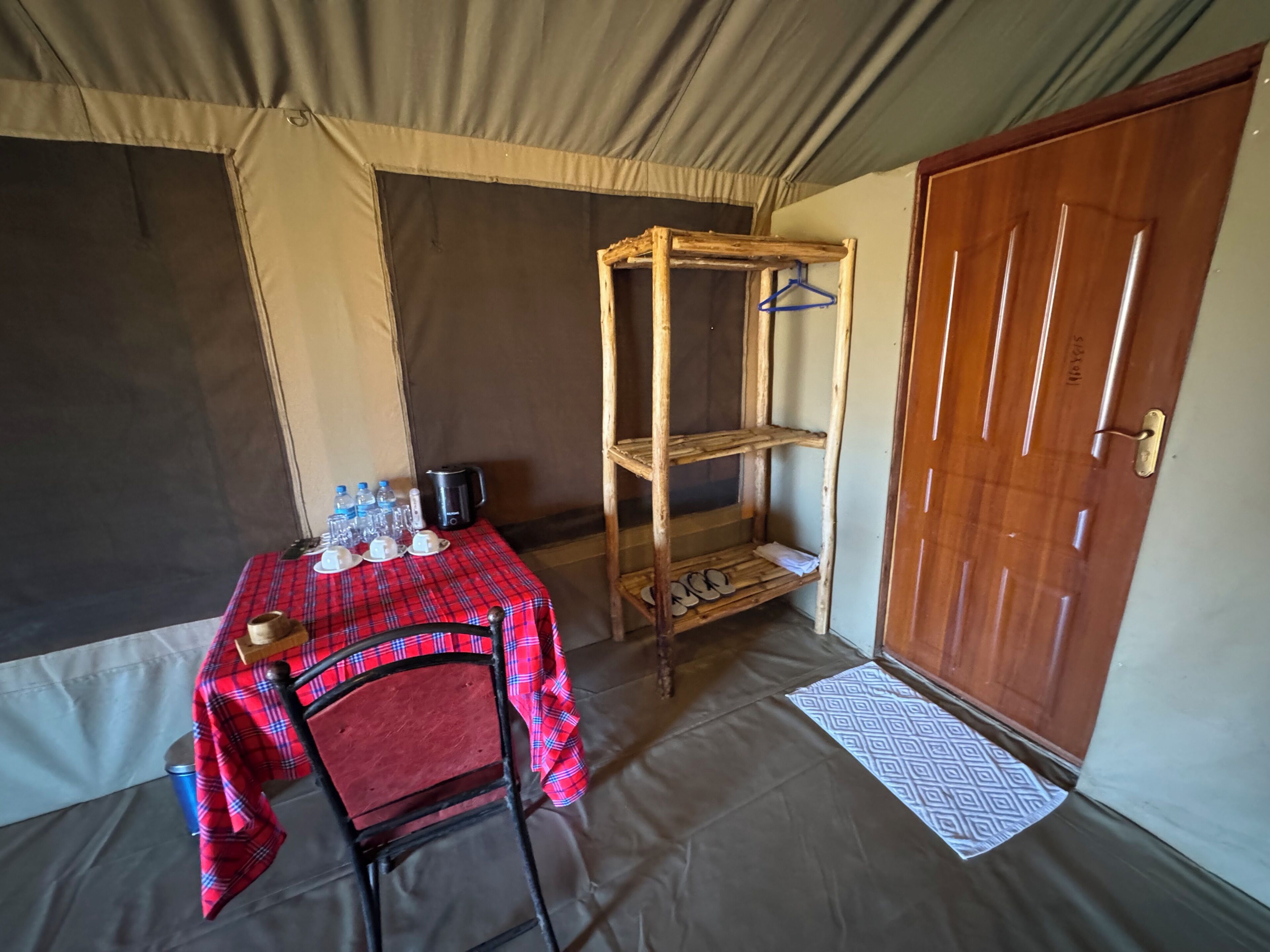 Una habitación con una mesa dispuesta para el desayuno, una silla, un estante de madera con perchas y una puerta.