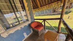 Una habitación con techo de paja, un sofá de mimbre, una pequeña mesa de madera y vistas a un jardín.