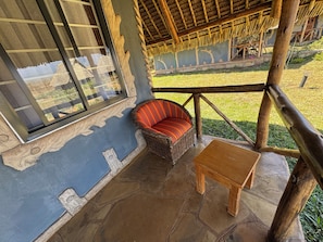 A room with a thatched roof, a wicker sofa, a small wooden table, and a view of a garden.