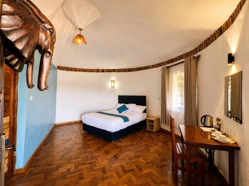 A hotel room with a bed, a dining table, a chair, a lamp, and a wall-mounted mirror.
