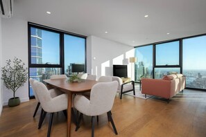 A modern living room with a dining table, sofas, and large windows offering a city view.