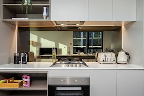 A modern kitchen with a gas stove, toaster, and kettle, a built-in oven, and a window with a view of the city.