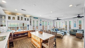 Eine geräumige Küche mit Holzausstattung, ein Essbereich mit Korbstühlen und ein Wohnzimmer mit blauem Sofa und Deckenventilator.