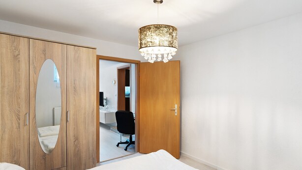 Une chambre à coucher avec une armoire en bois, un miroir, un lit, un bureau et une chaise.