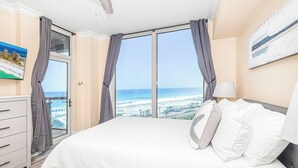 Une chambre à coucher avec un grand lit, une table de chevet, une lampe et un tableau représentant une scène de plage.