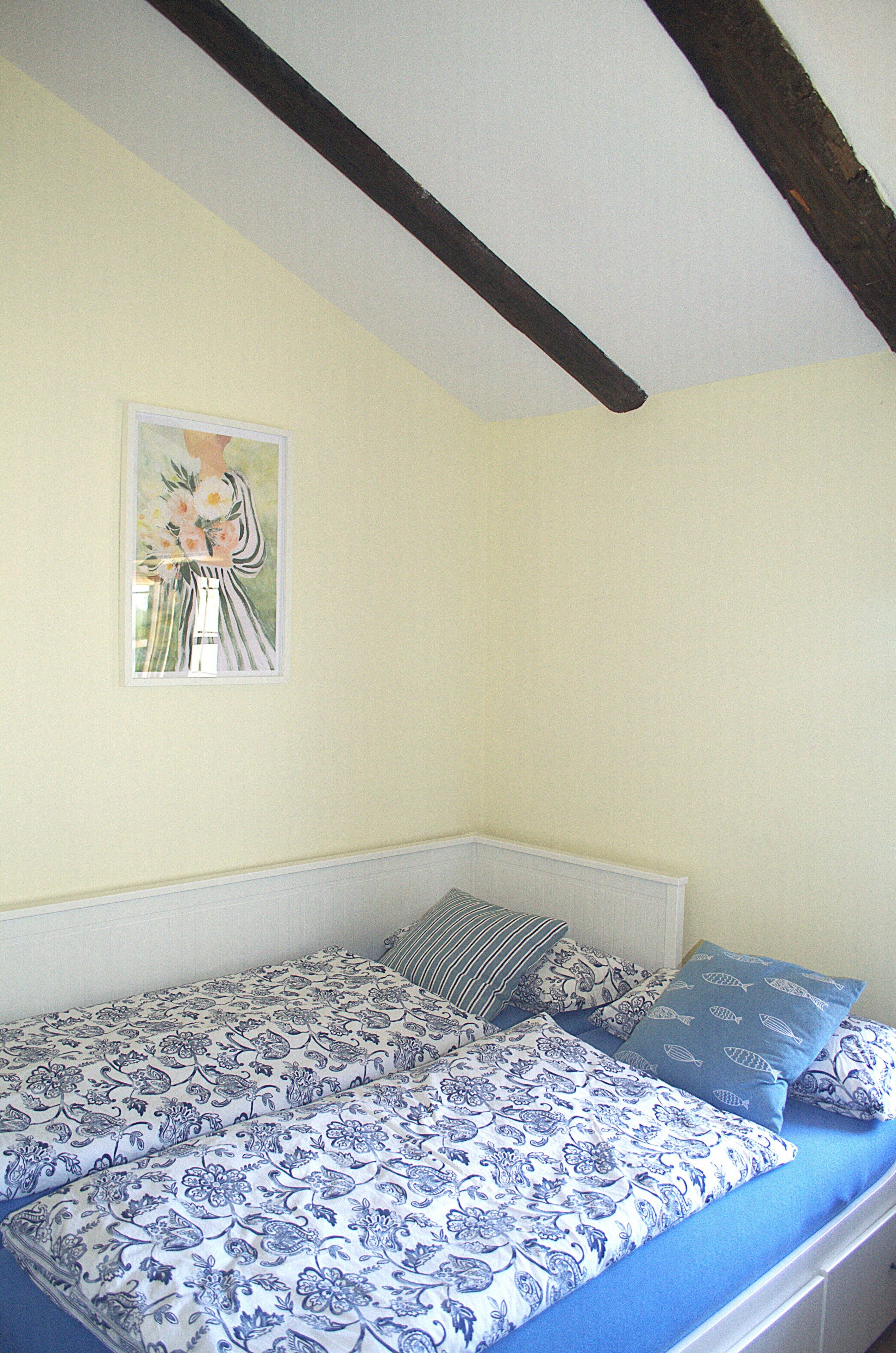Quarto com cama, almofadas, um quadro e teto inclinado.