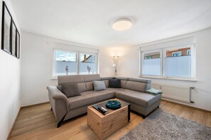A modern living room with a sectional sofa, a wooden coffee table, and a large window with blinds.