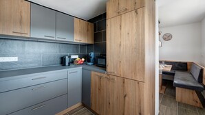 A modern kitchen with grey cabinets, a wooden accent wall, a built-in microwave, and a small dining area with a bench. - Ferienwohnung Schäfer – Nature, Comfort & Relaxation in the Black Forest (Freudenstadt)