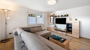 A modern living room with a sofa, TV, wooden cabinets, and a floor lamp. - Ferienwohnung Schäfer – Nature, Comfort & Relaxation in the Black Forest (Freudenstadt)